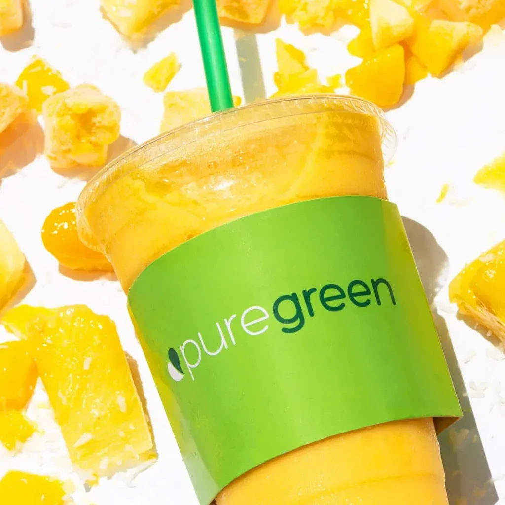 A mango Pure Green smoothie surrounded by fresh fruit